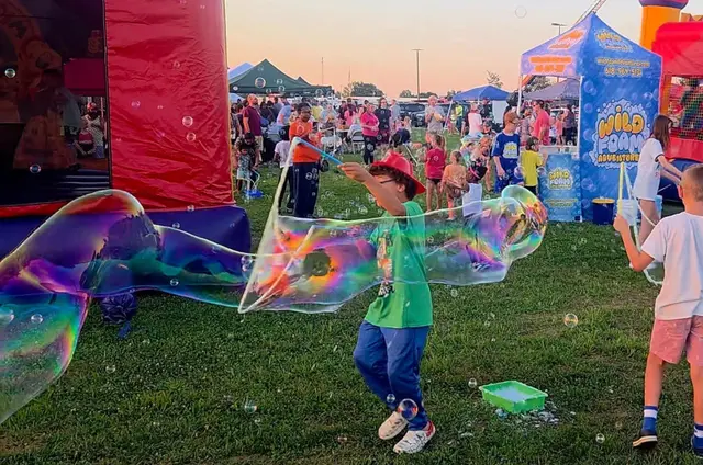 A child chasing a giant rainbow bubble at an outdoor event
