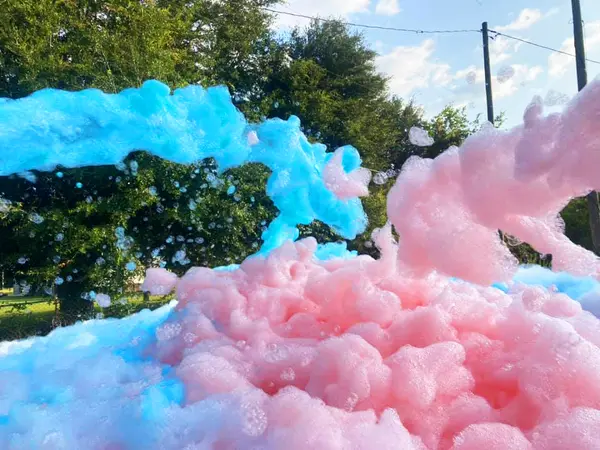 A cannon pouring blue and pink coloured foam across a lawn